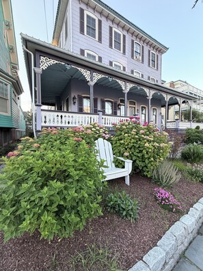A two-story house with a porch, a white Adirondack chair, and a garden with various plants and flowers. - 1 Block from Cape May Beach & 10 min. walking distance to mall- 3rd Floor Unit (Cape May)