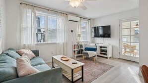 Ein Wohnzimmer mit Sofa, Couchtisch, Fernseher, Bücherregal und Blick durch eine Glastür.