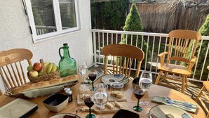 Mesa de comedor al aire libre con sillas, una cesta de frutas, hogaza de pan, copas de vino y cubiertos.