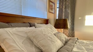 Una cama con ropa de cama blanca, cabecera de madera y cortina estampada.
