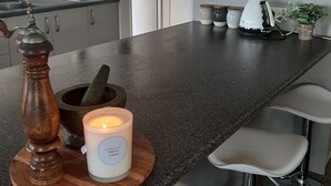 Cozinha com bancada de granito, moedor de pimenta de madeira, pilão e almofariz, uma vela acesa e uma cafeteira.