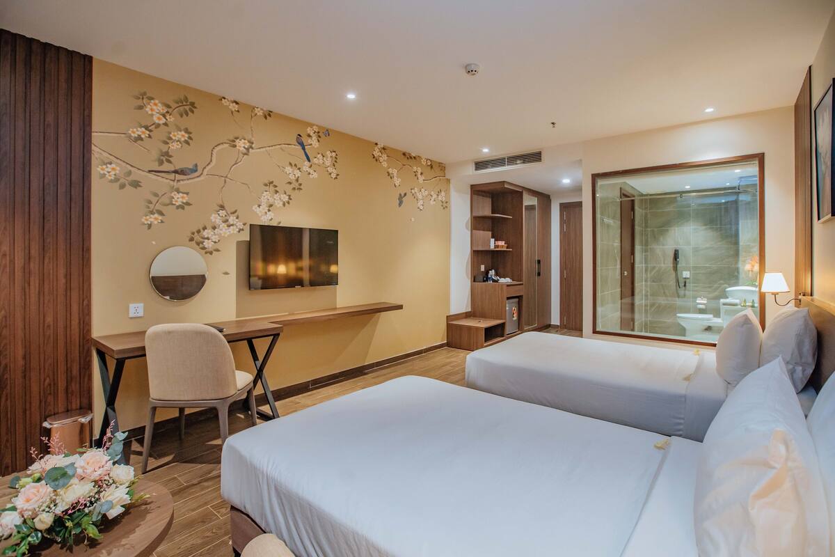 Hotelkamer met twee bedden, een bureau, een stoel, een televisie, een kledingkast en een badkamer zichtbaar door een glazen deur.