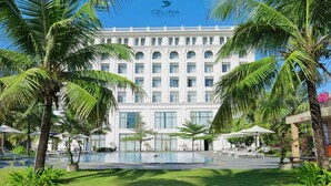 A hotel with a large pool, surrounded by palm trees and a well-maintained lawn. - Celina Peninsula Resort (Dong Hoi)
