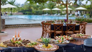 An outdoor dining area with tables set for a buffet, overlooking a pool and surrounded by palm trees. - Celina Peninsula Resort (Dong Hoi)