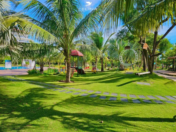A well-maintained park with palm trees, a playground, and a Ferris wheel. - Celina Peninsula Resort (Dong Hoi)