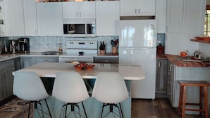 A modern kitchen with white cabinets, a central island with bar stools, a built-in oven, and a refrigerator. - Miller's Landing (Traverse City)