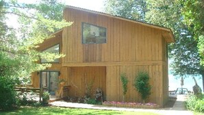A wooden cabin with a large window, a door, and a small porch area with plants. - Miller's Landing (Traverse City)