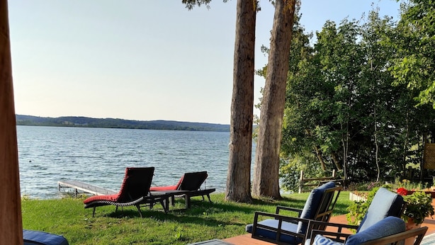 A wooden deck with outdoor furniture, including chairs and tables, overlooking a lake. - Miller's Landing (Traverse City)