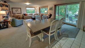 A spacious living room with a large dining table, comfortable seating, and a view of the outdoors through large windows. - Miller's Landing (Traverse City)