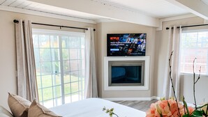 Een slaapkamer met een bed, gordijnen, een aan de muur bevestigde televisie en een raam.