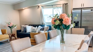 Een moderne keuken met een marmeren aanrechtblad, roestvrijstalen apparatuur en een eethoek met een witte tafel en beige stoelen.
