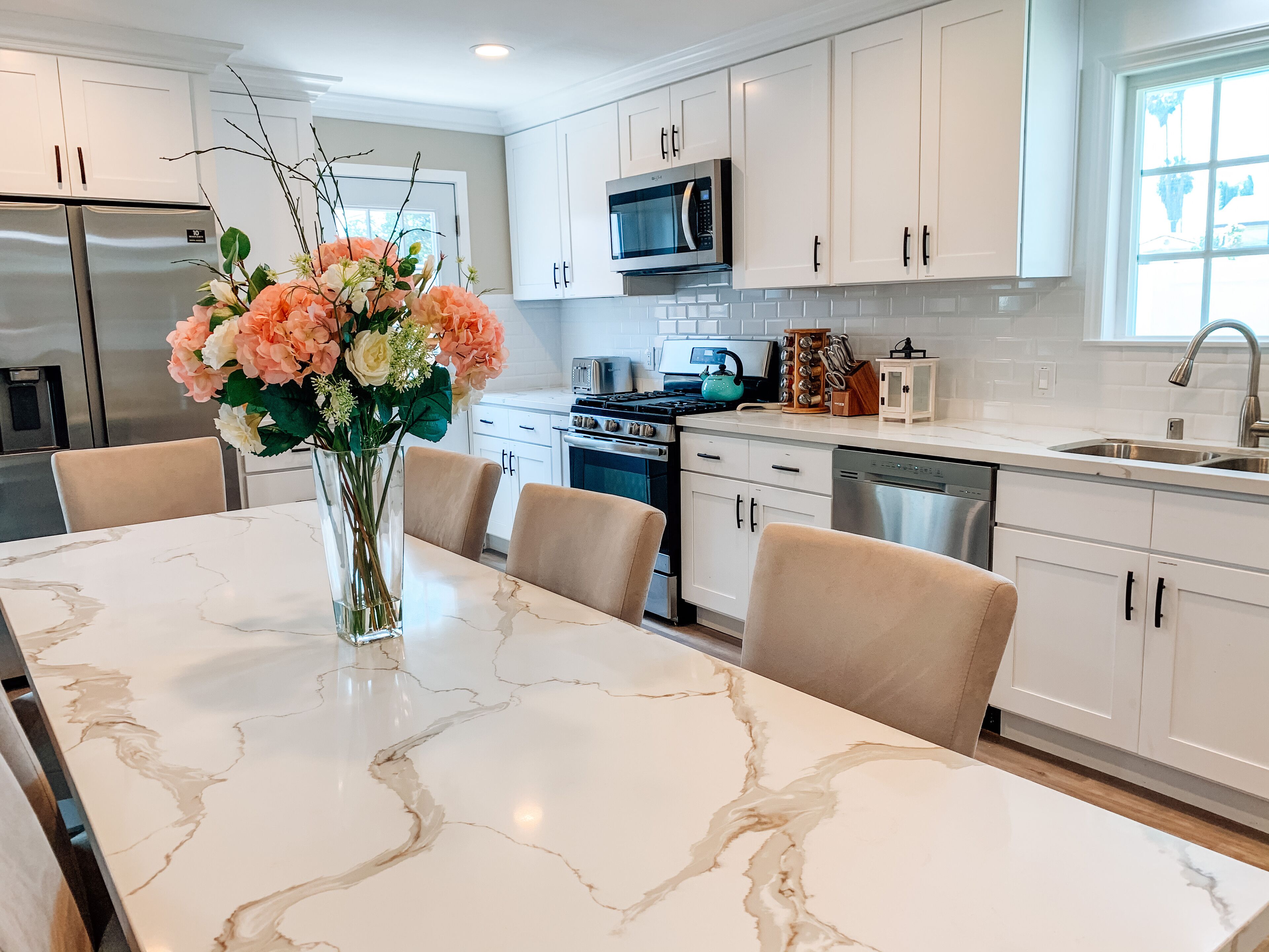 A modern kitchen with white cabinets, a marble island, and a vase of flowers.