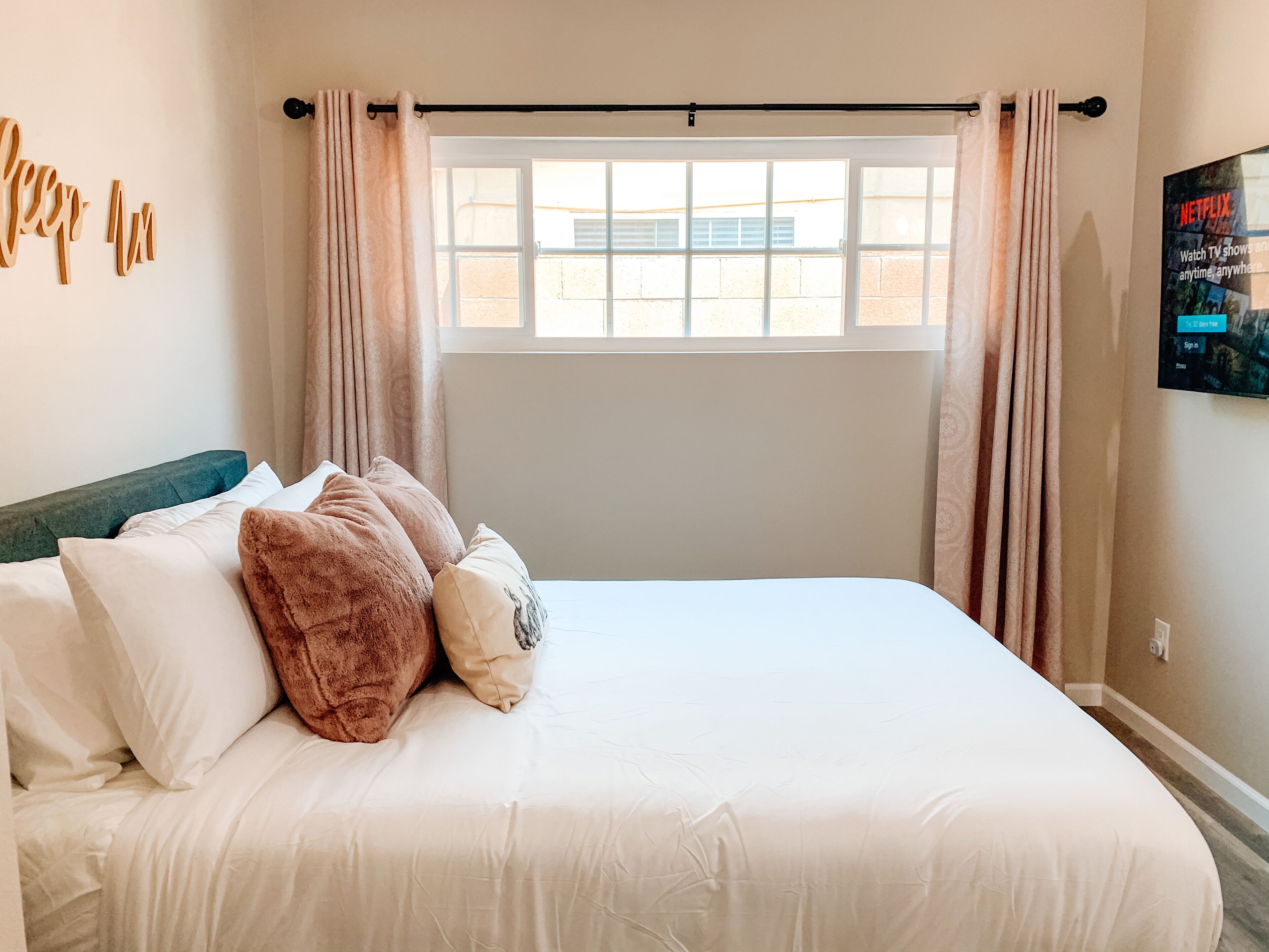 A neatly made bed with white and brown pillows, a teal headboard, and a window with curtains.