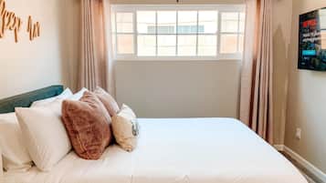 A neatly made bed with white and brown pillows, a teal headboard, and a window with curtains.