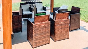 Een terras buiten met rieten meubels en een barbecue.