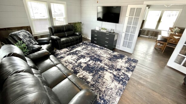 Ein Wohnzimmer mit einem Ecksofa, einem Fernseher, einem Deckenventilator und einem großen Fenster.