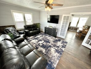 A living room with a sectional sofa, a TV, a ceiling fan, and a large window.