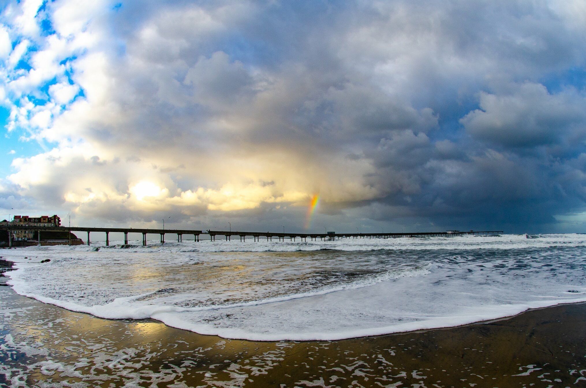 A beach with a pier extending into the sea, under a cloudy sky.