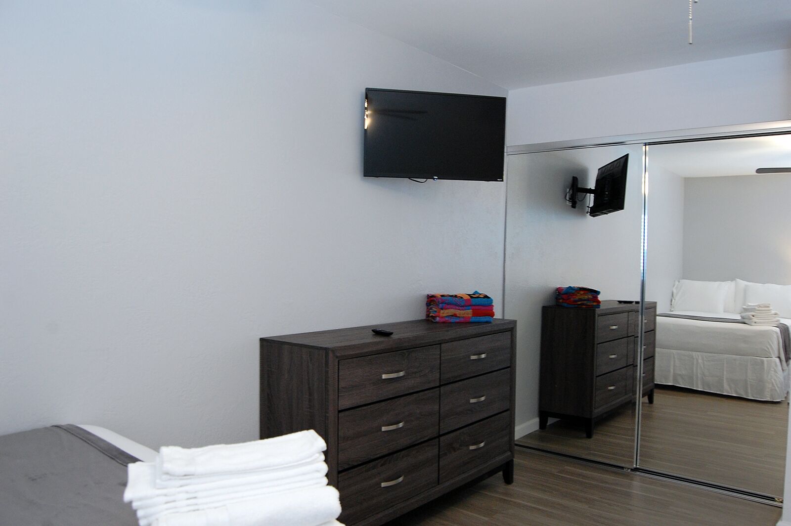 Una camera da letto moderna con una cassettiera in legno scuro, una TV a schermo piatto montata a parete e un grande specchio che riflette l'ambiente.