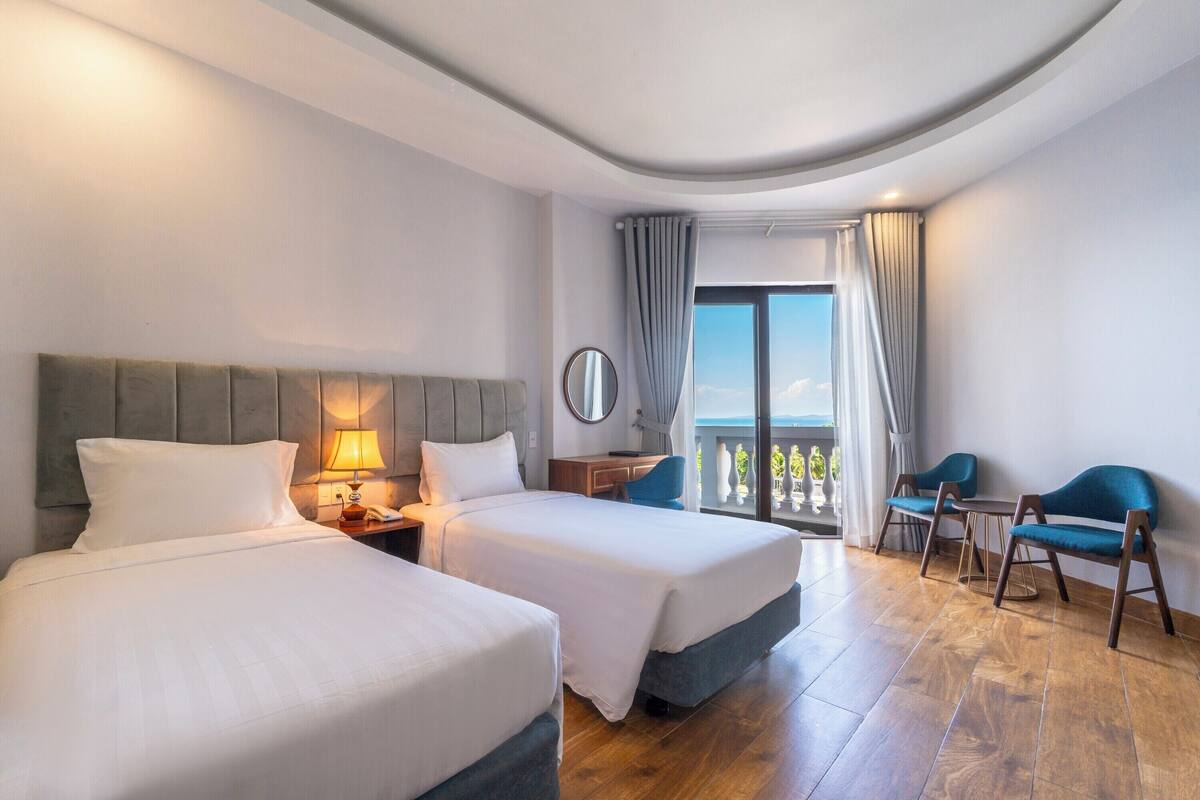 Ett hotellrum med två sängar, ett skrivbord, en stol och en balkong med utsikt.