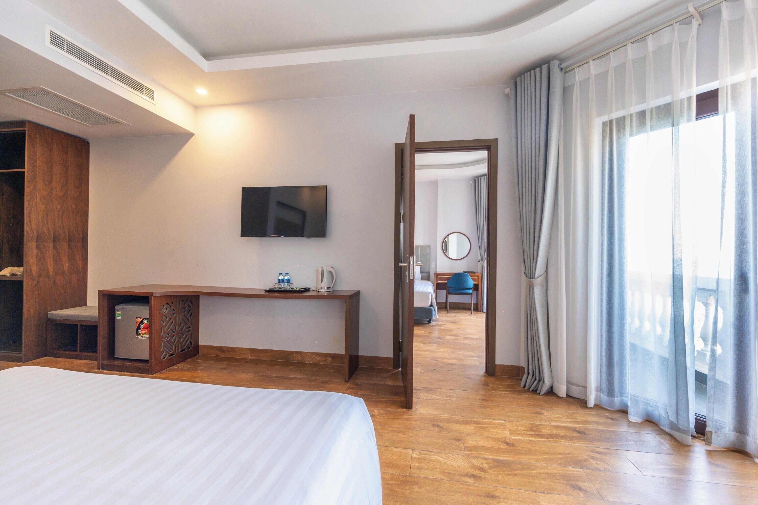 A hotel room with a bed, a desk with a television, a wardrobe, and a view of the balcony.