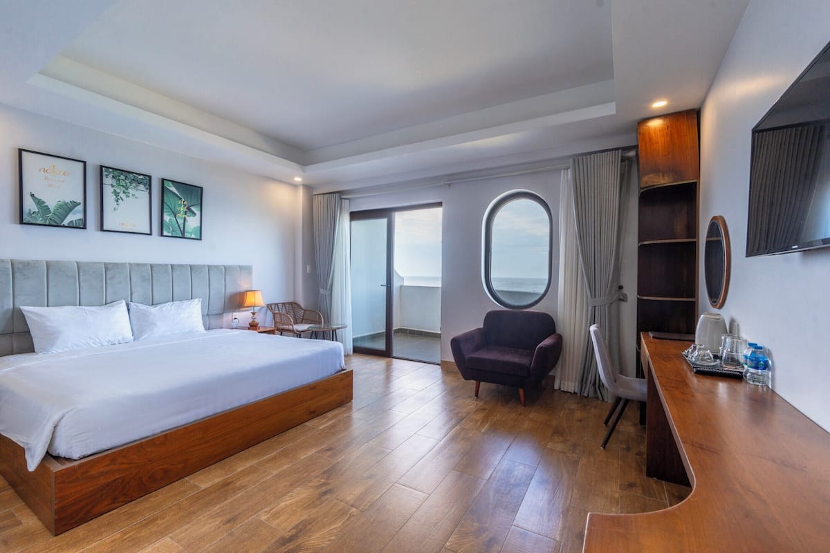Ett modernt hotellrum med en stor säng, ett skrivbord, en stol och utsikt över himlen genom ett fönster.