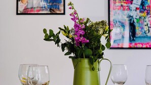 A dining table with a green tablecloth, a green pitcher with flowers, and two framed artworks on the wall.