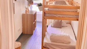 A bunk bed with a wooden frame, a desk with a chair, a small plant, and a basket on the floor.