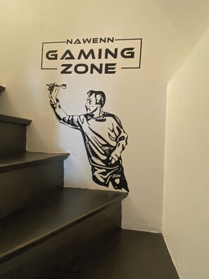 A wall with a sign reading 'NAWENN GAMING ZONE' and a black and white illustration of a person holding a dart. - Billard, Déco Tendance & Détente Entre Terre et mer (La Landec)
