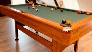 A pool table with balls, a person playing, and a brick wall in the background.