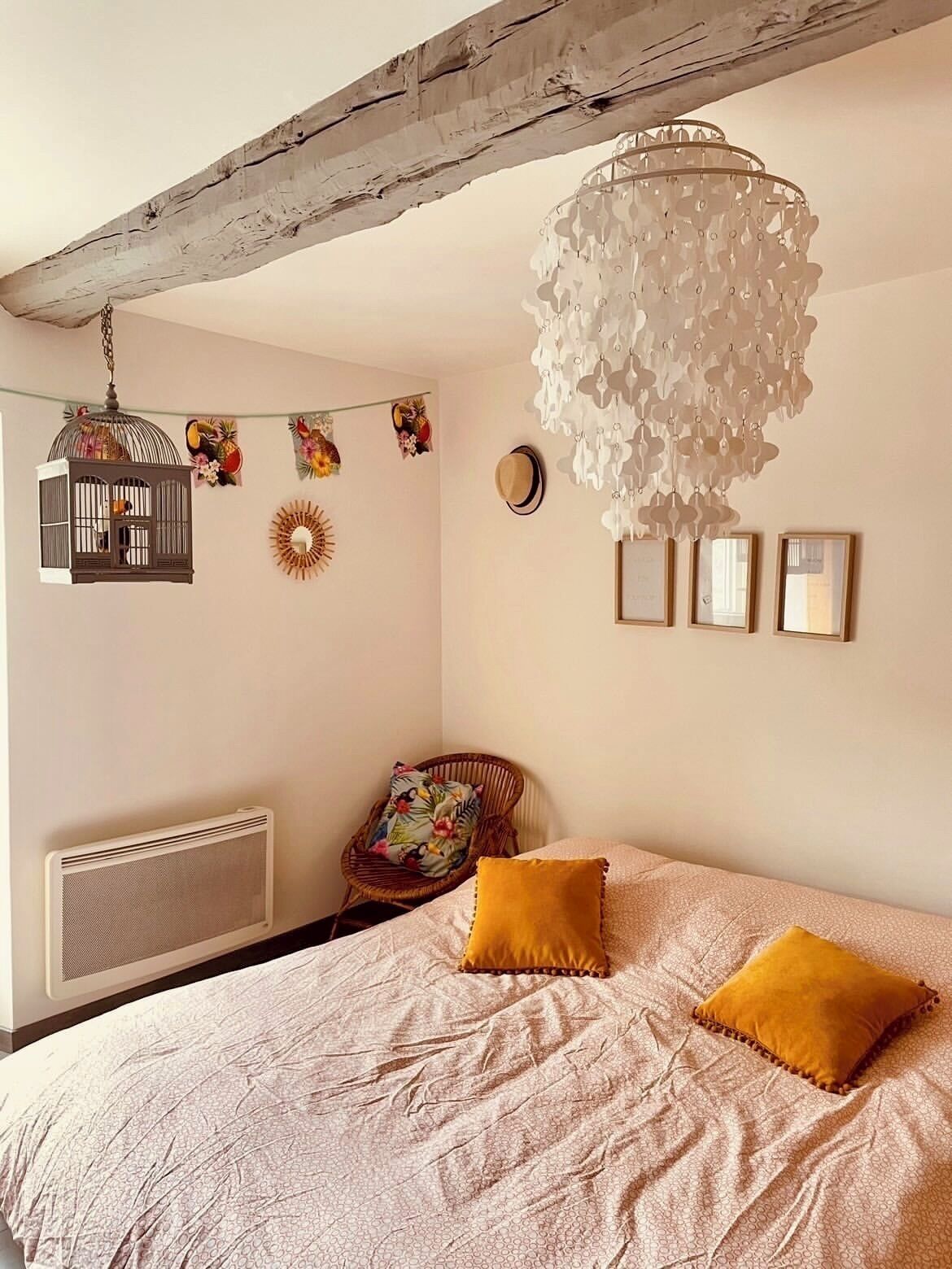 Une chambre à coucher comprenant un lit, un luminaire suspendu, un radiateur, une chaise et des éléments décoratifs sur les murs.