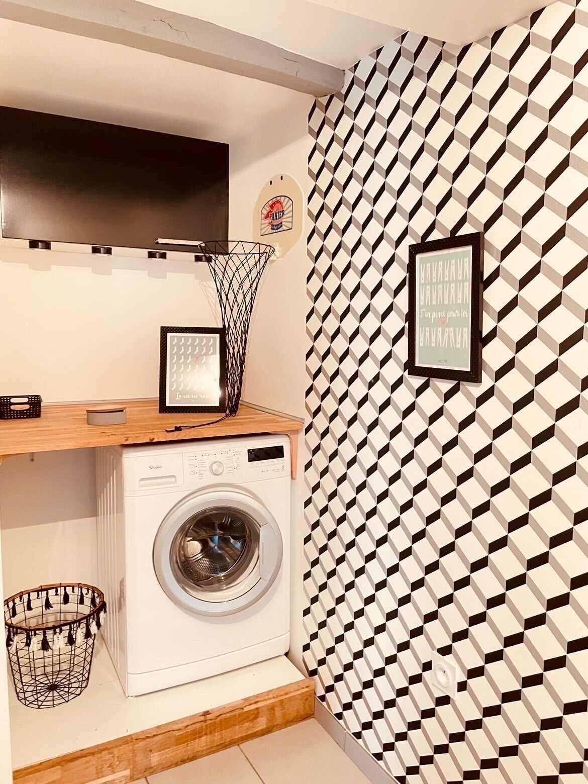 Un espace buanderie comprenant un lave-linge, un étendoir et un téléviseur fixé au mur.