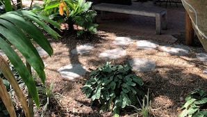 Ein  überdachter Außenbereich mit einem Reetdach, umgeben von üppiger Vegetation und einer Steinmauer.