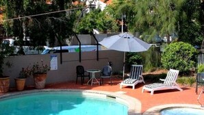 Ein Schwimmbecken mit Liegestühlen und einem Tisch, umgeben von Blumentöpfen und einem Zaun.