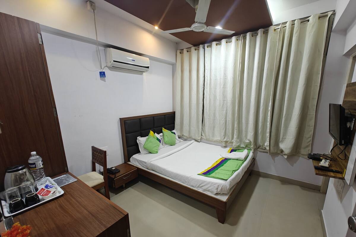 A hotel room with a bed, a desk with a water bottle, a remote control, and a TV.