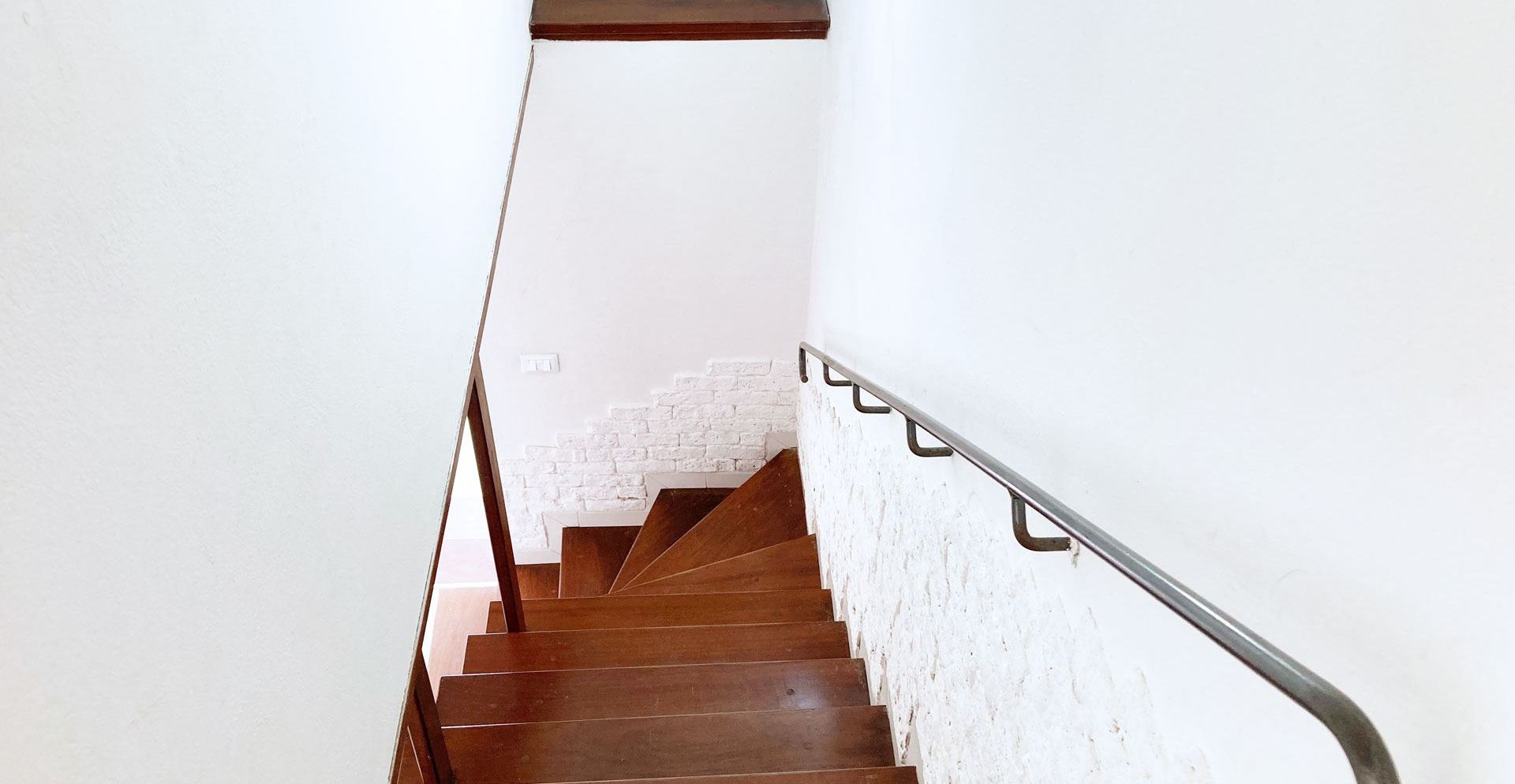 Un escalier en bois, avec des murs blancs et une rampe en métal.