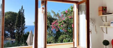 A room with a large window offering a view of the sea and trees.