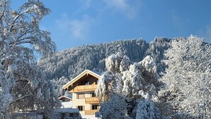 Ett snötäckt landskap med ett trähus, träd och en klarblå himmel.