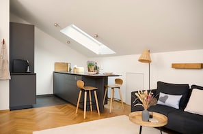 Et moderne køkken med ovenlys, mørkegrå skabe, træborde og en sort sofa med en hjertepude.