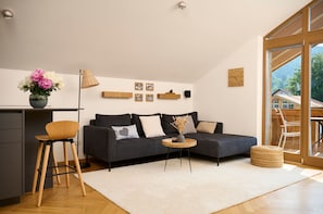 En moderne stue med sofa, et lille rundt bord, en skammel og en vase med blomster.