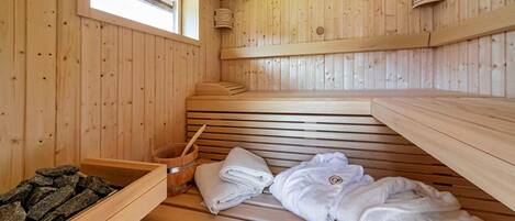 Una sala de sauna con bancos de madera, una ventana, un cubo de madera y toallas.