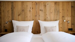 A double bed with white bedding, wooden headboard, bedside tables with lamps, and a small nightstand. - Ferienappartement Haferlschuh - Alpenseensucht Natur-ferienappartements (Bad Wiessee)