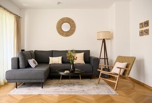 A living room with a grey sofa, a round coffee table, a floor lamp, a wicker chair, and a wall-mounted mirror.
