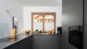 A modern kitchen with a built-in oven, a sink, and a window with a view of a building. - Ferienappartement Haferlschuh - Alpenseensucht Natur-ferienappartements (Bad Wiessee)