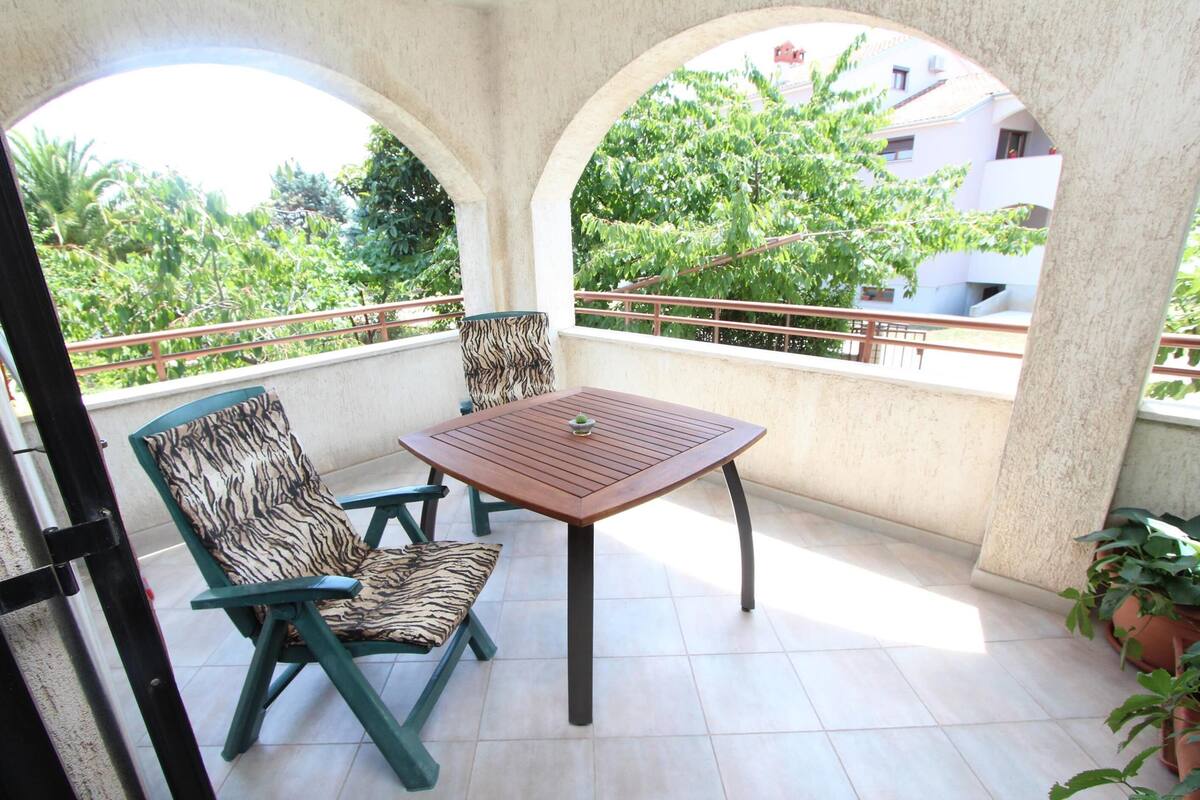 A balcony with two chairs and a table, surrounded by arches and a railing.