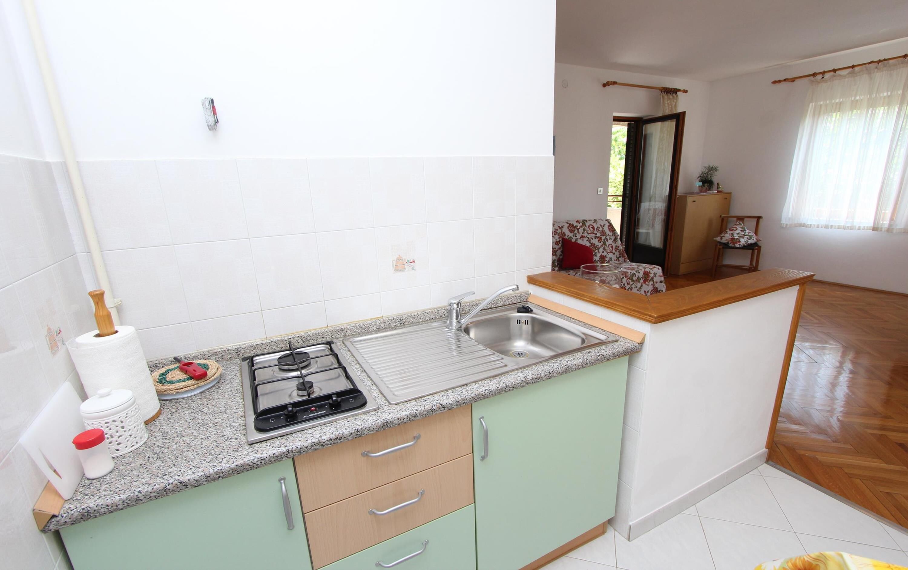 Una cocina compacta con estufa a gas, lavamanos y gabinetes verde claro.