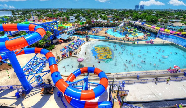 Parque acuático con toboganes y piscinas, rodeado de sillas y sombrillas de playa.