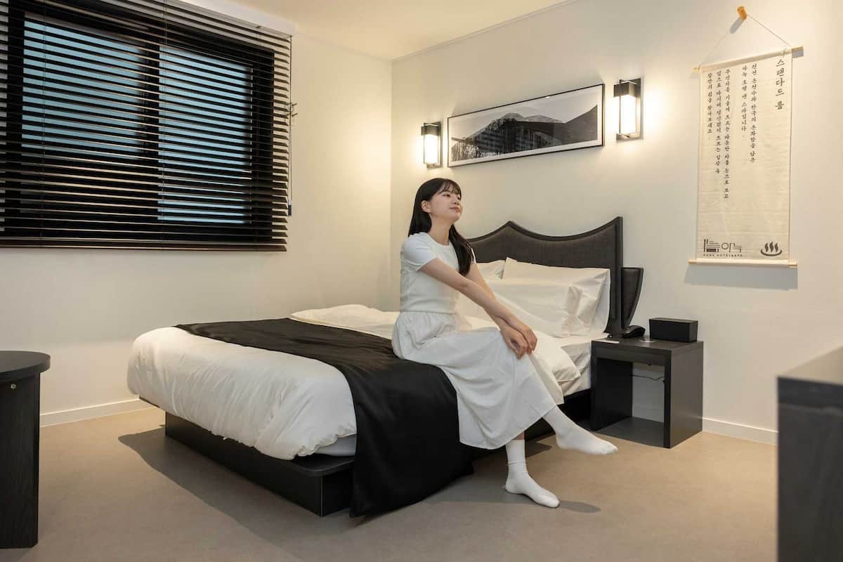 Een moderne hotelkamer met een bed, een nachtkastje, een wandlamp en een lijst met een afbeelding.