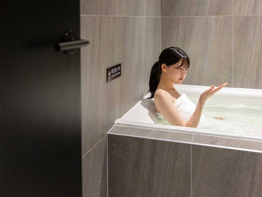 A person in a bathtub with a caution sign on the wall.