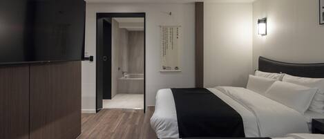 Ein modernes Hotelzimmer mit zwei Betten, einem Flachbildfernseher, einem Holzschrank, einem Badezimmer mit Badewanne sowie einer wandmontierten Lampe.